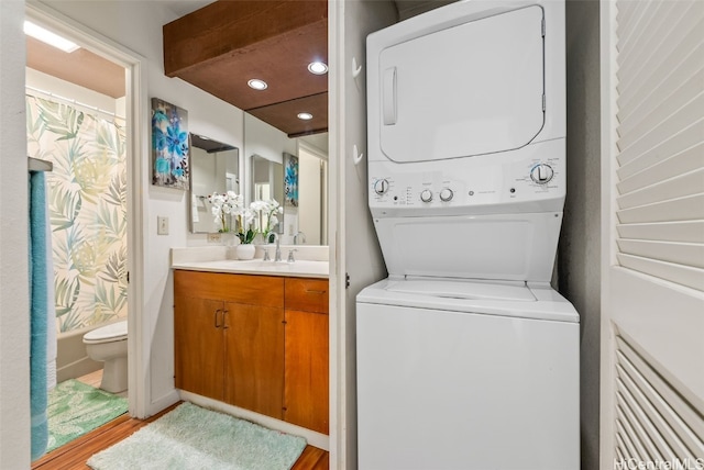 clothes washing area with sink, stacked washer and dryer, and light wood-type flooring