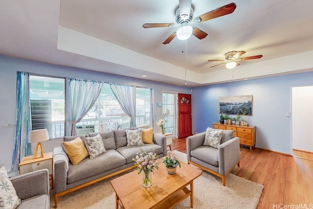 living room with light hardwood / wood-style floors, a raised ceiling, and ceiling fan