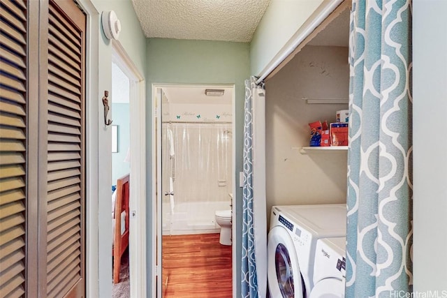 washroom with a textured ceiling, laundry area, separate washer and dryer, and wood finished floors