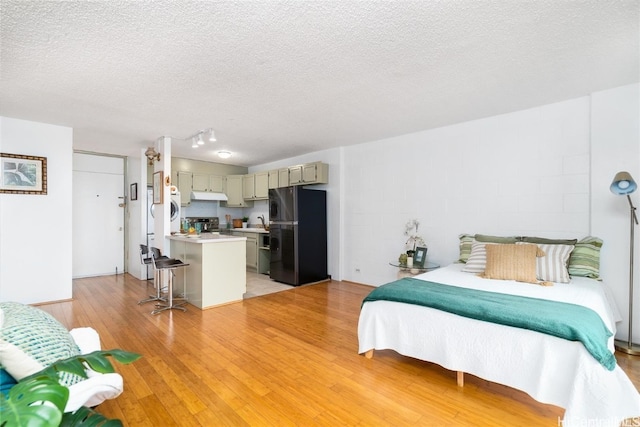 bedroom with black fridge, sink, white refrigerator, a textured ceiling, and light hardwood / wood-style floors