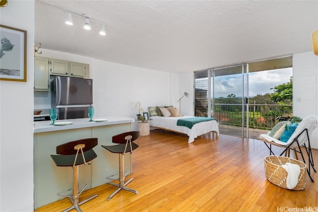 bedroom with access to exterior, light hardwood / wood-style flooring, a textured ceiling, and stainless steel refrigerator