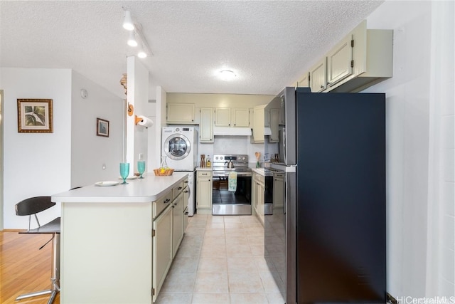 kitchen featuring washer / dryer, cream cabinets, light tile patterned floors, appliances with stainless steel finishes, and a textured ceiling