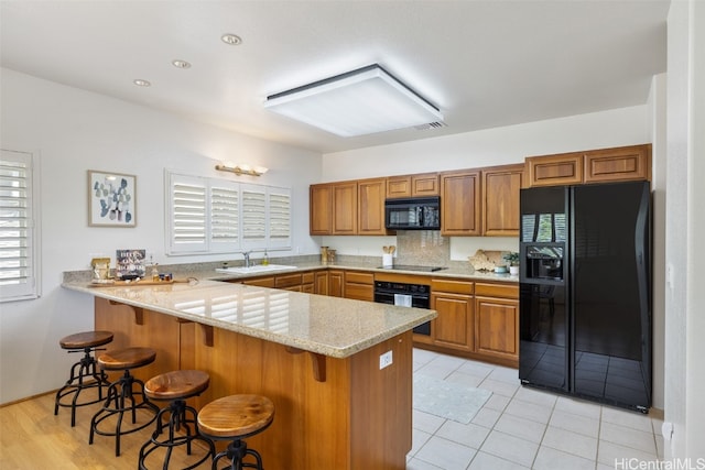 kitchen featuring kitchen peninsula, black appliances, sink, a kitchen bar, and light stone counters