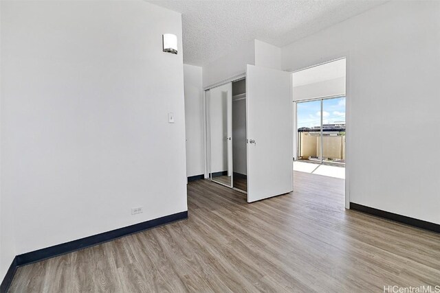 spare room featuring light wood finished floors, baseboards, and a textured ceiling