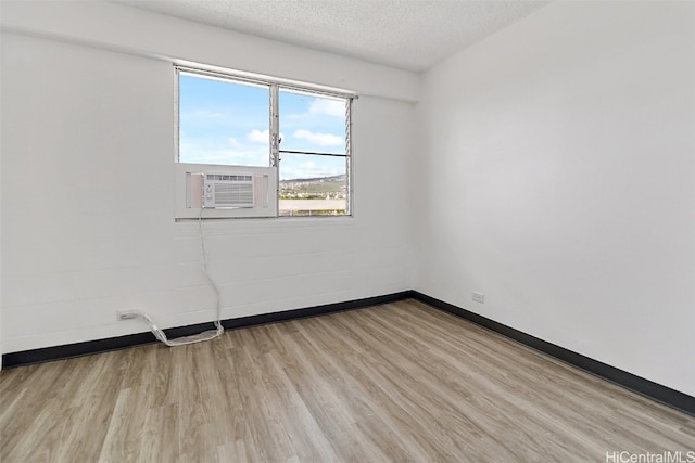 empty room featuring a textured ceiling, light wood finished floors, cooling unit, and baseboards
