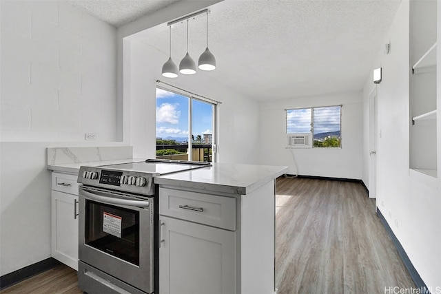 kitchen with a wealth of natural light, pendant lighting, stainless steel electric stove, and a textured ceiling