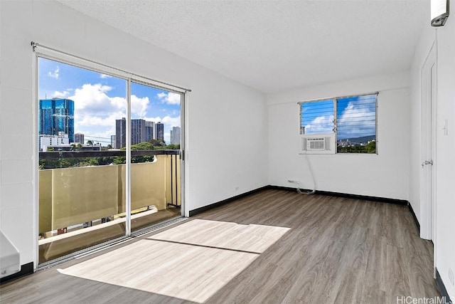spare room with a textured ceiling, cooling unit, a city view, wood finished floors, and baseboards