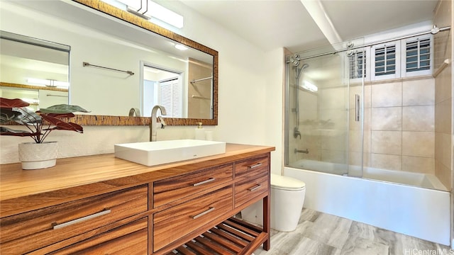 full bathroom featuring toilet, combined bath / shower with glass door, and vanity