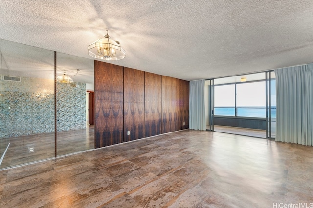 spare room featuring a textured ceiling, concrete flooring, wooden walls, a water view, and a notable chandelier