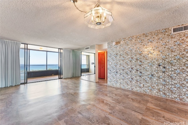 unfurnished room featuring a textured ceiling, a notable chandelier, a water view, and expansive windows