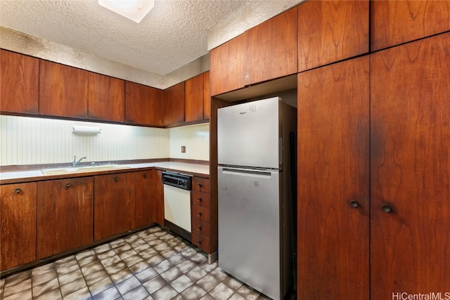 kitchen featuring white dishwasher, sink, a textured ceiling, and stainless steel refrigerator