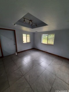 tiled empty room featuring a raised ceiling and plenty of natural light