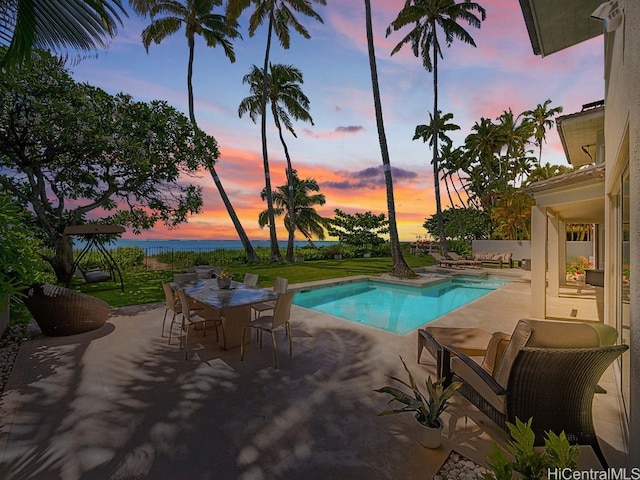 pool at dusk featuring a water view, a yard, and a patio