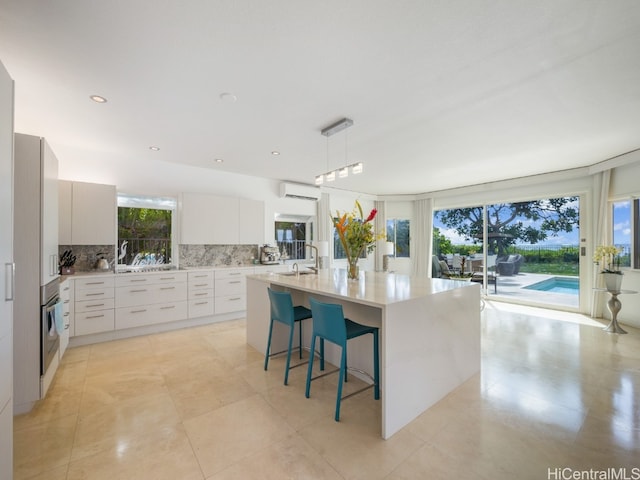 kitchen with an AC wall unit, a kitchen breakfast bar, hanging light fixtures, white cabinets, and tasteful backsplash