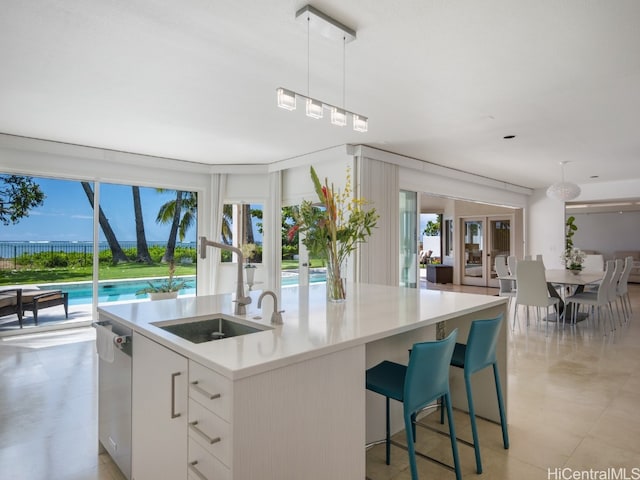 kitchen with dishwasher, a center island with sink, sink, decorative light fixtures, and white cabinetry