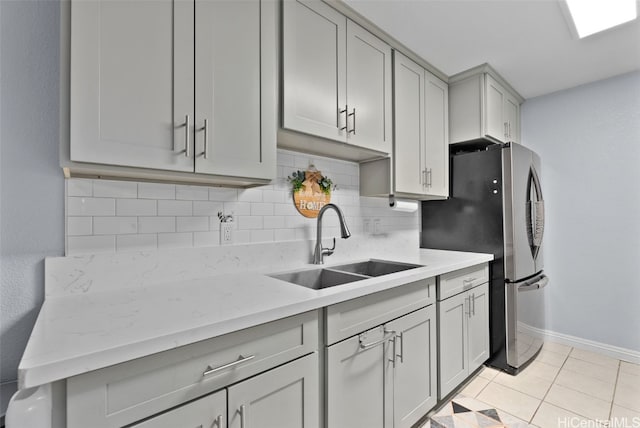 kitchen with sink, gray cabinets, decorative backsplash, light tile patterned floors, and stainless steel refrigerator