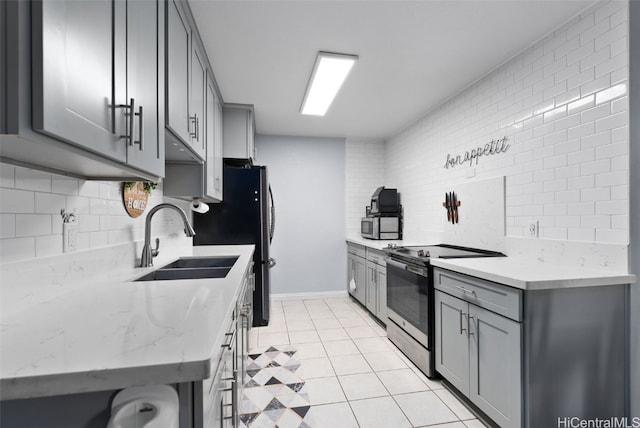 kitchen featuring light tile patterned floors, appliances with stainless steel finishes, backsplash, light stone countertops, and sink