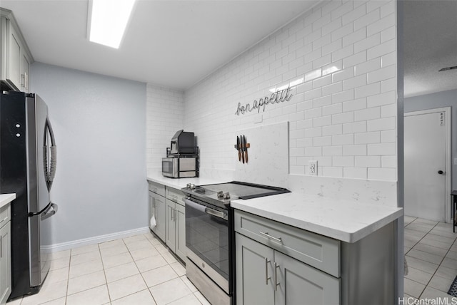 kitchen featuring tasteful backsplash, light tile patterned floors, appliances with stainless steel finishes, gray cabinets, and light stone counters