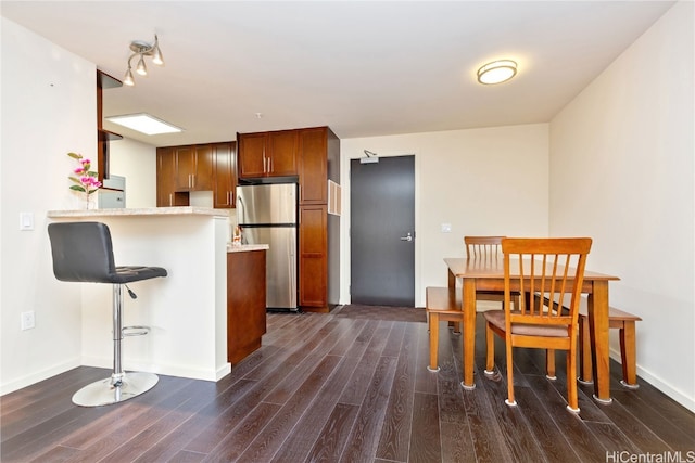 kitchen with kitchen peninsula, stainless steel fridge, a kitchen bar, and dark hardwood / wood-style floors