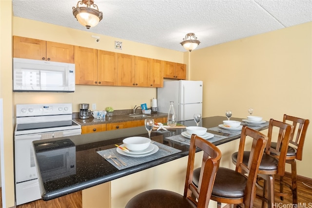 kitchen with a kitchen breakfast bar, a textured ceiling, dark wood-type flooring, sink, and white appliances