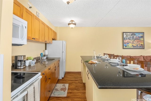 kitchen with hardwood / wood-style floors, a breakfast bar, a textured ceiling, sink, and white appliances