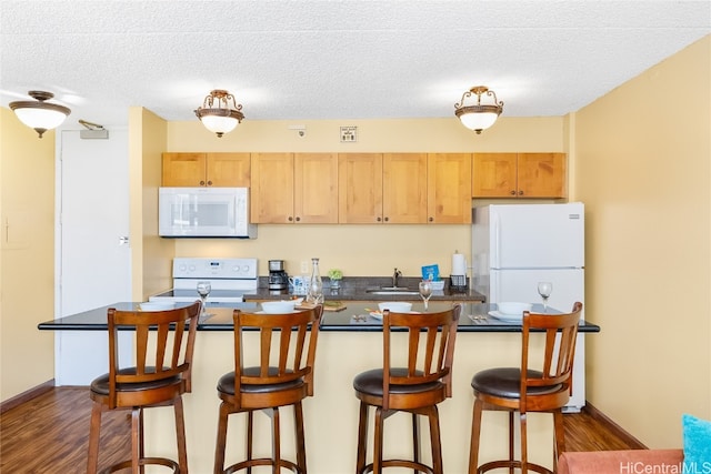 kitchen featuring light brown cabinets, dark hardwood / wood-style floors, a breakfast bar, a textured ceiling, and white appliances