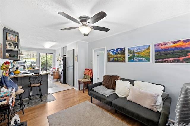 living room featuring ceiling fan, bar, a textured ceiling, and light wood-type flooring