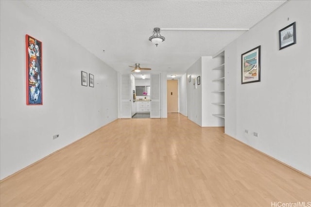 unfurnished living room with light wood-style flooring, built in shelves, a ceiling fan, and a textured ceiling