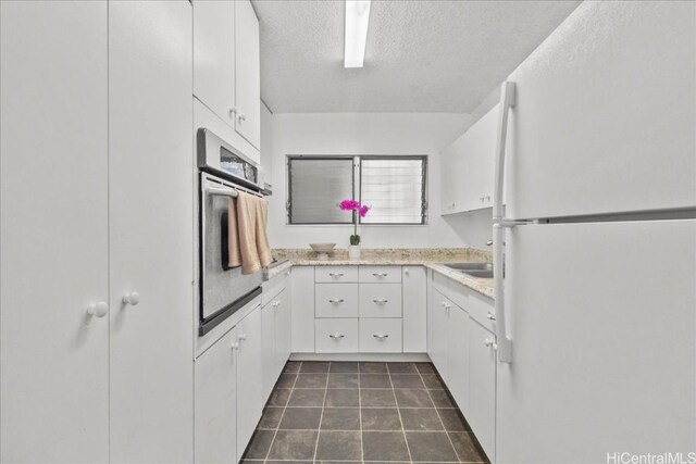 kitchen with stainless steel oven, white cabinetry, white fridge, and a textured ceiling