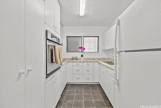 kitchen with light countertops, stainless steel oven, freestanding refrigerator, and white cabinetry