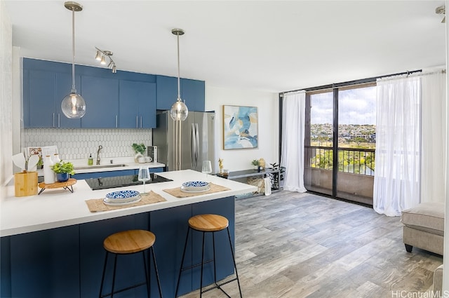 kitchen featuring blue cabinetry, tasteful backsplash, kitchen peninsula, stainless steel fridge, and light hardwood / wood-style floors