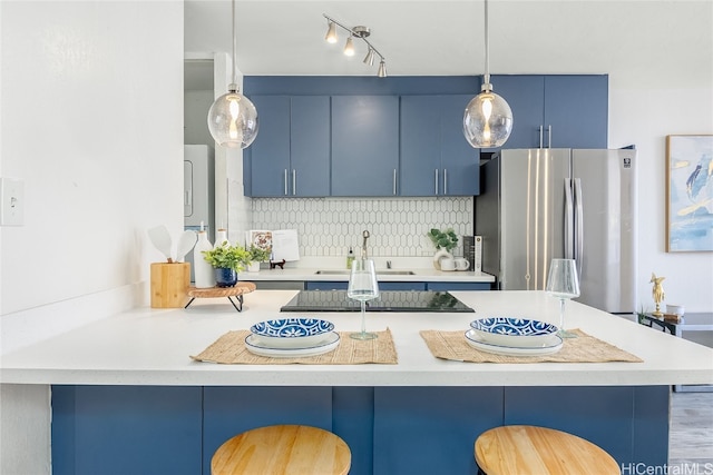 kitchen featuring a kitchen bar, stainless steel fridge, backsplash, blue cabinets, and hanging light fixtures