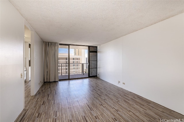 unfurnished room featuring a wall of windows, wood-type flooring, and a textured ceiling