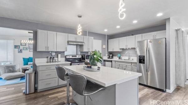 kitchen with pendant lighting, a center island, sink, hardwood / wood-style flooring, and appliances with stainless steel finishes