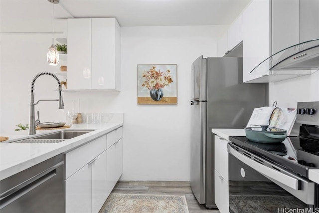 kitchen with appliances with stainless steel finishes, sink, light hardwood / wood-style flooring, white cabinets, and hanging light fixtures