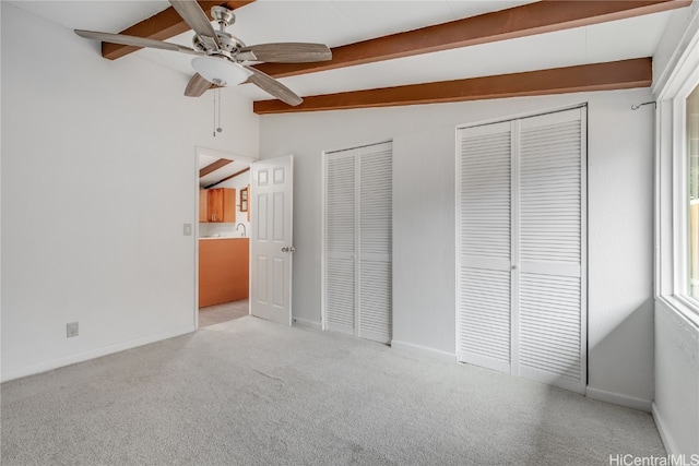 unfurnished bedroom with light carpet, vaulted ceiling with beams, ceiling fan, and multiple closets