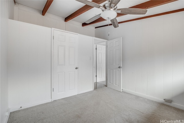 unfurnished bedroom with carpet floors, ceiling fan, and beamed ceiling