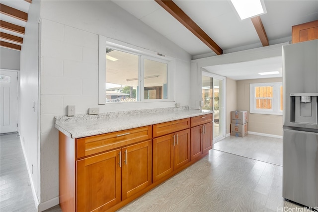 kitchen featuring stainless steel fridge, vaulted ceiling with beams, light hardwood / wood-style floors, and plenty of natural light