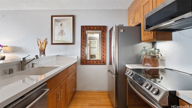 kitchen featuring a textured ceiling, light stone countertops, sink, light hardwood / wood-style floors, and stainless steel appliances