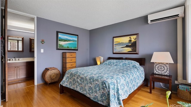 bedroom with ensuite bathroom, a textured ceiling, a wall mounted AC, and light wood-type flooring