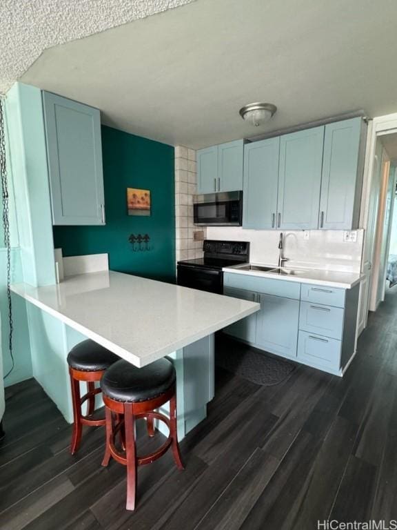 kitchen featuring dark wood-style floors, decorative backsplash, light countertops, stainless steel microwave, and black electric range oven