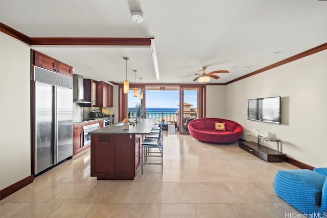 kitchen featuring ceiling fan, a center island, wall chimney exhaust hood, hanging light fixtures, and appliances with stainless steel finishes