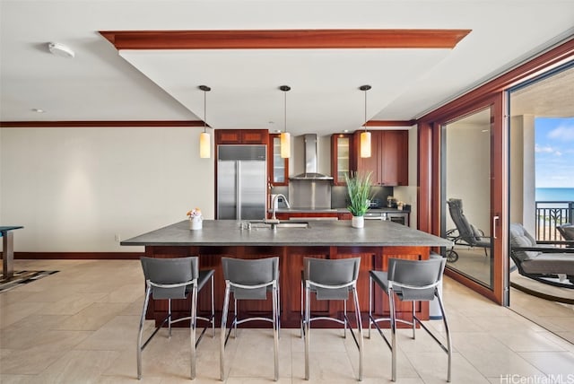 kitchen featuring built in fridge, decorative light fixtures, wall chimney range hood, and sink