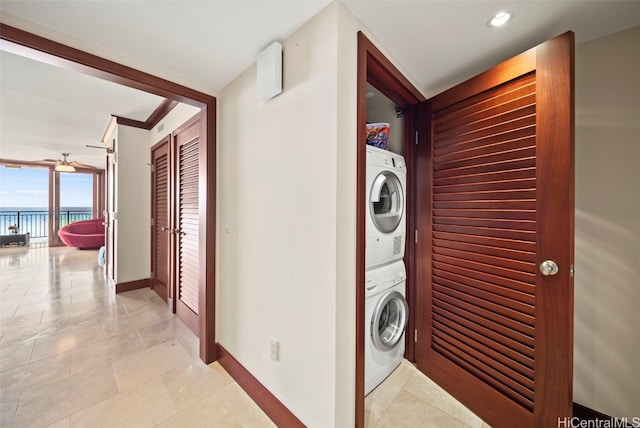 clothes washing area with light tile patterned floors, a water view, ceiling fan, and stacked washer / drying machine