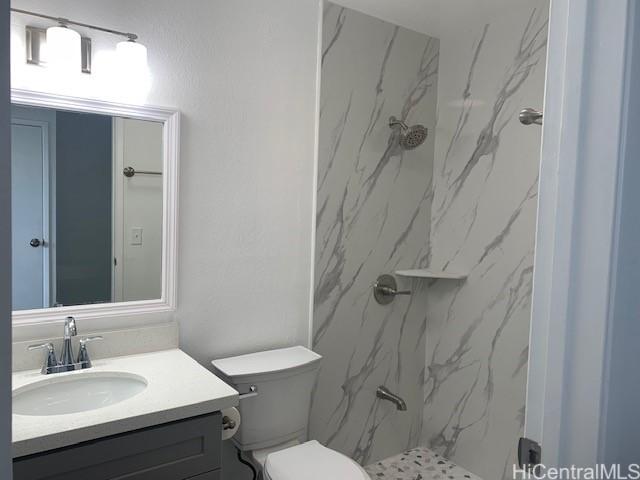 bathroom with toilet, vanity, and a marble finish shower