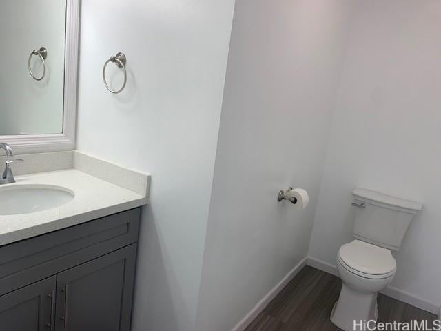 bathroom with toilet, vanity, wood finished floors, and baseboards