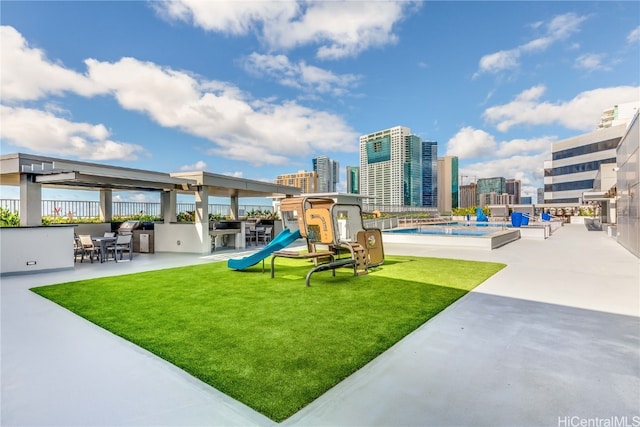 view of play area with a patio, a community pool, and a lawn