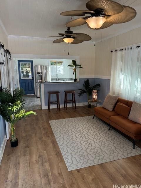 living area featuring ornamental molding, a barn door, a ceiling fan, and wood finished floors