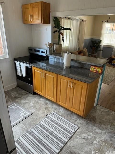 kitchen with stainless steel electric range oven, open floor plan, dark stone countertops, and brown cabinets