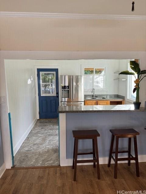 bar featuring crown molding, wood finished floors, a sink, stainless steel fridge, and baseboards